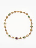 A gold link bracelet featuring multiple colored gemstone settings, including emerald-cut green emeralds, round-cut red garnet-like stones, light blue stones, a square purple amethyst, and clear pavé-set diamonds, displayed on a clean white background.