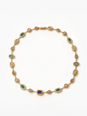 A gold link bracelet featuring multiple colored gemstone settings, including emerald-cut green emeralds, round-cut red garnet-like stones, light blue stones, a square purple amethyst, and clear pavé-set diamonds, displayed on a clean white background.